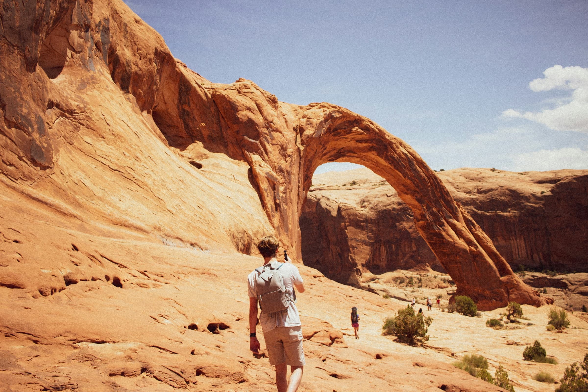 A hiker walking toward a sandstone arch in Moab