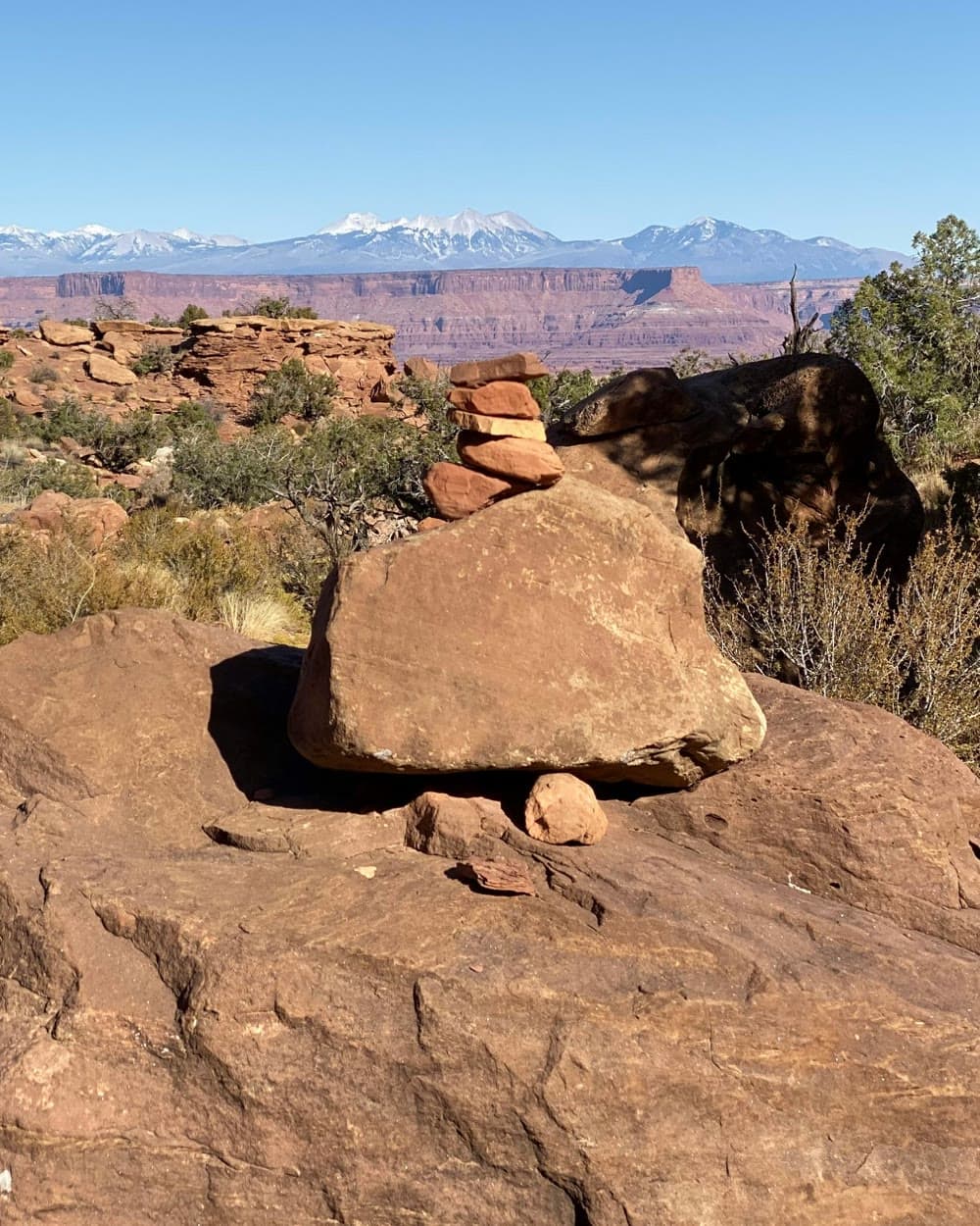 A cairn of stacked red rocks with snow-capped mountains beyond