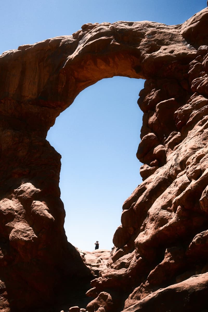 A hiker beneath a towering sandstone arch