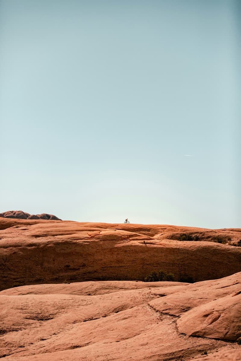A lone figure walking a slickrock ridge under a pale sky